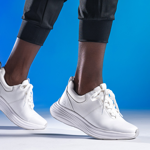 Woman wearing the Align™ Tulia in White, with her heels lifted slightly in a forward motion. Shot on a blue background