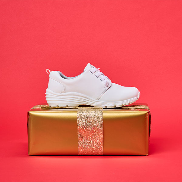 Women’s Align™ Velocity sneaker in White sitting on a gold wrapped present on a red background. Shop Align™ Velocity sneaker in white.