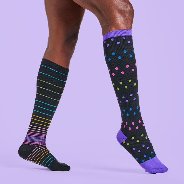 Woman wearing two different patterned compression socks in black with her front foot slightly in the air